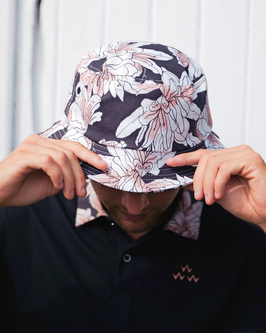 A person wearing a dark azalea print bucket hat and a matching floral collar polo shirt.