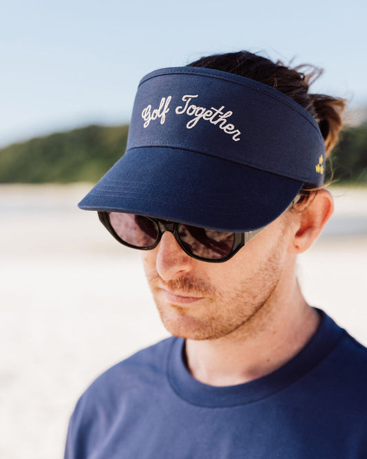 A man wearing a navy visor with embroidered white script text across the front and sunglasses.