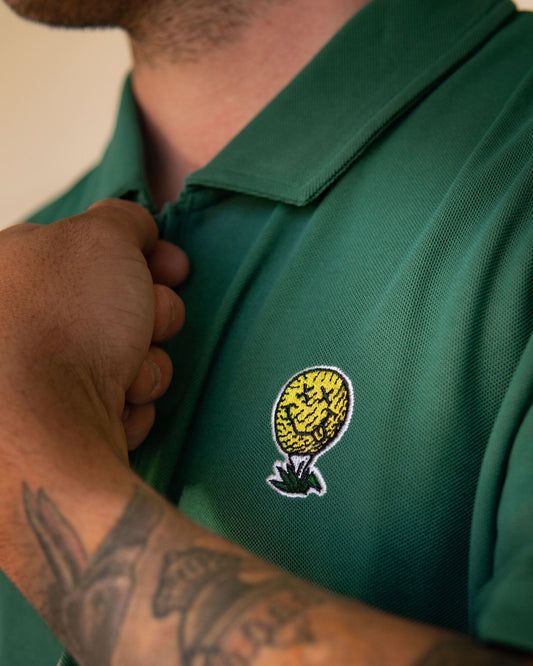 Detail of a man wearing a green polo shirt with an embroidered yellow golf ball graphic on the chest.