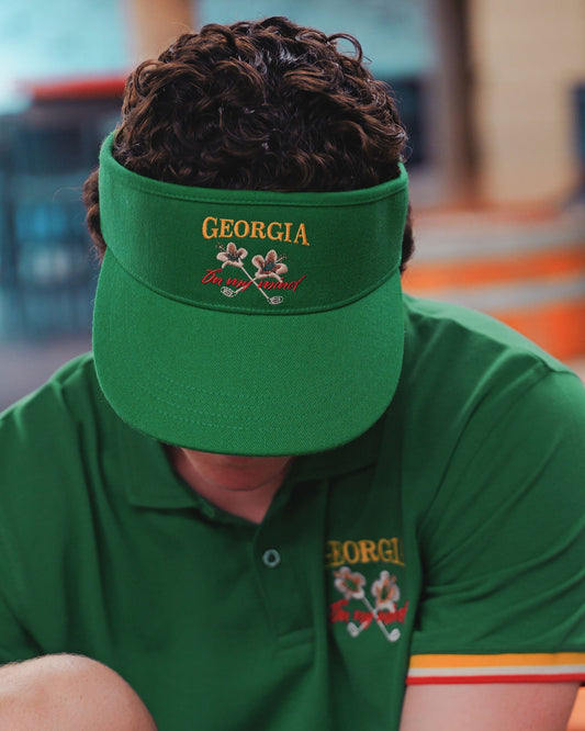 A person wearing a Masters Green tour visor with a yellow and red Georgia On My Mind golf motif.