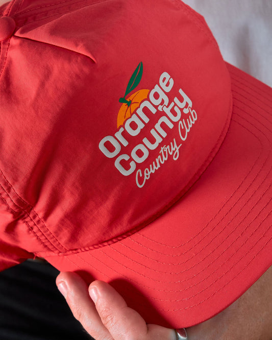 Detail of a blood orange nylon cap with an orange and green Orange County Club graphic.
