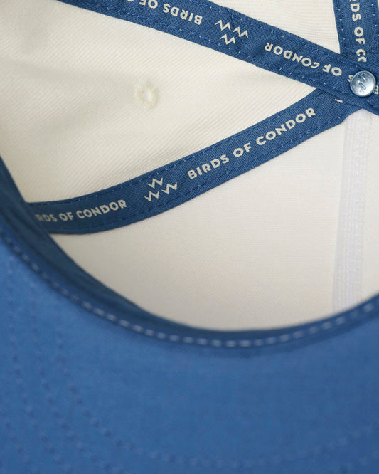 Detail of an off-white snapback cap interior, showing blue contrast taping with white text and branding.