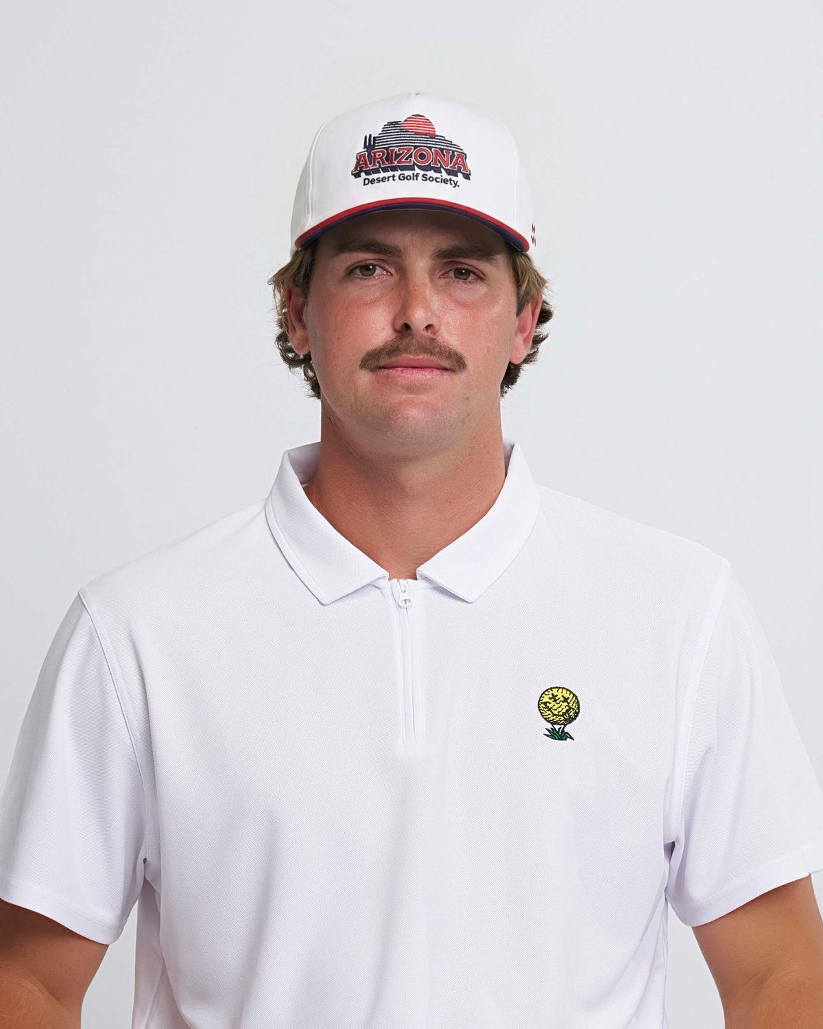 Man wearing a white polo shirt with a neverfind golf logo and a cap with 'Arizona Desert Golf Society' text on a plain background