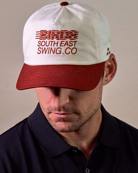 A man wearing a natural white snapback with red wine brim and a text logo.