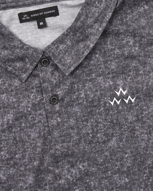 Detail of acid black polo shirt with white triple eagle logo, collar, and branded dark buttons.