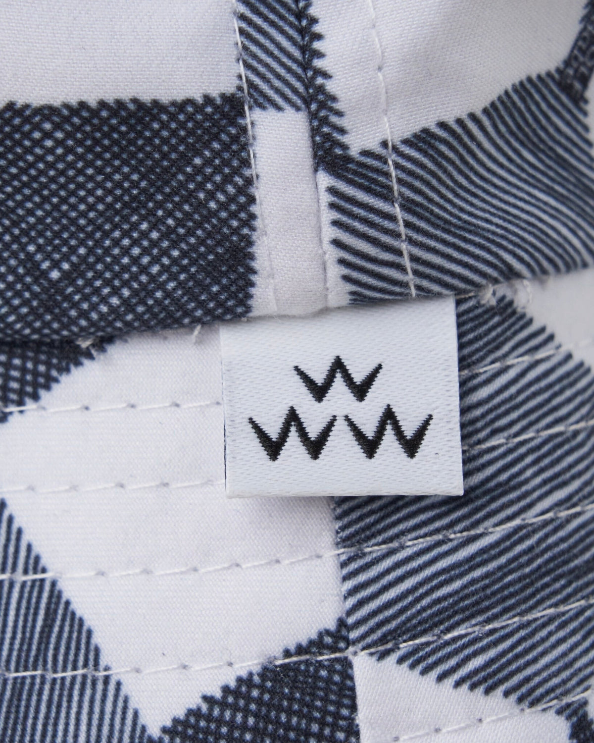 Detail of a black and white gingham bucket hat featuring a white brand tag with three W symbols.