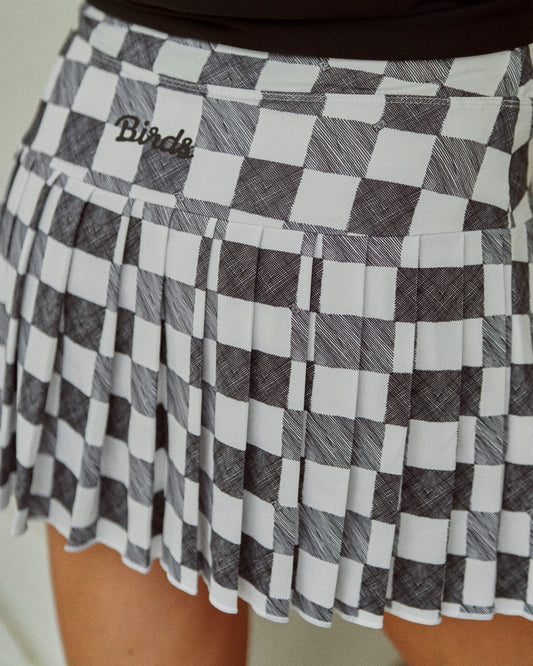 Back of a black and white gingham pleated skort with a white script Birds logo on the waistband.