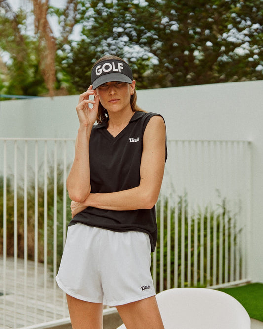 A woman wearing white shorts with a black birds print, a black top, and a black visor with text.