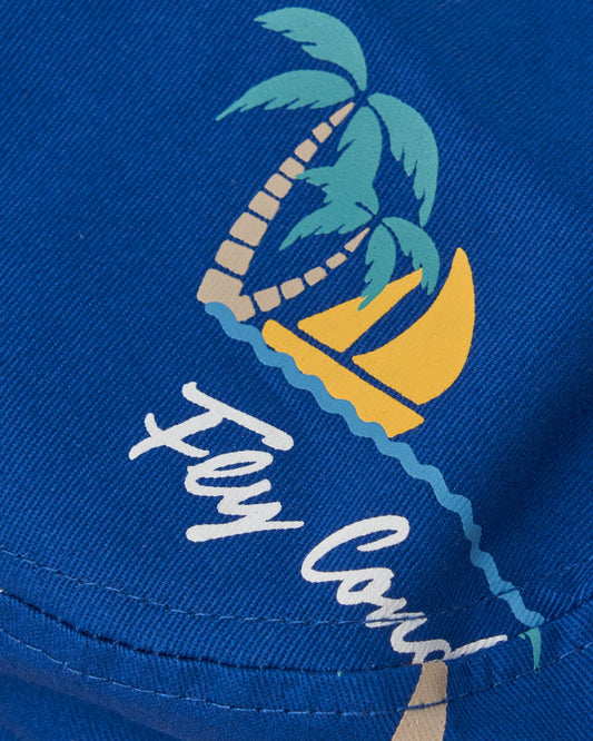 Detail of a blue bucket hat featuring a repeat design of palm trees, a yellow sailboat, and text.
