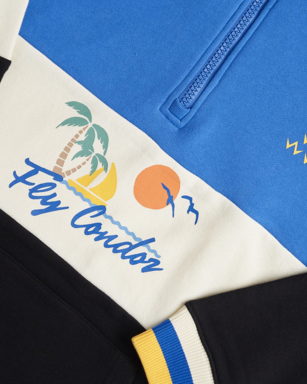 Detail of a blue, off-white, and black sweater featuring a quarter-zip and a tropical beach graphic.