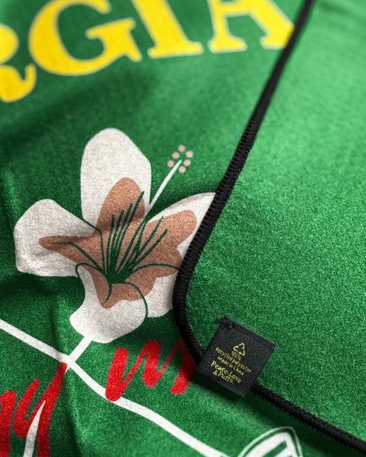 Detail of a green golf towel with a waffle texture, a white flower graphic, and yellow text.
