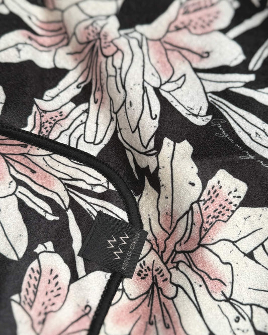 Detail of an azalea pink and black golf towel with an all-over floral print and a small black label.