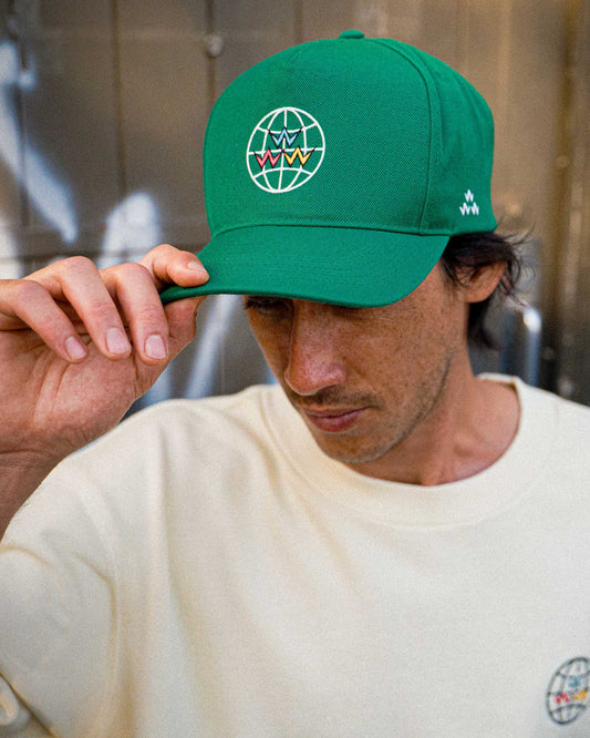 A man wearing a green 5-panel snapback hat with a white globe and multi-coloured flying V logo.