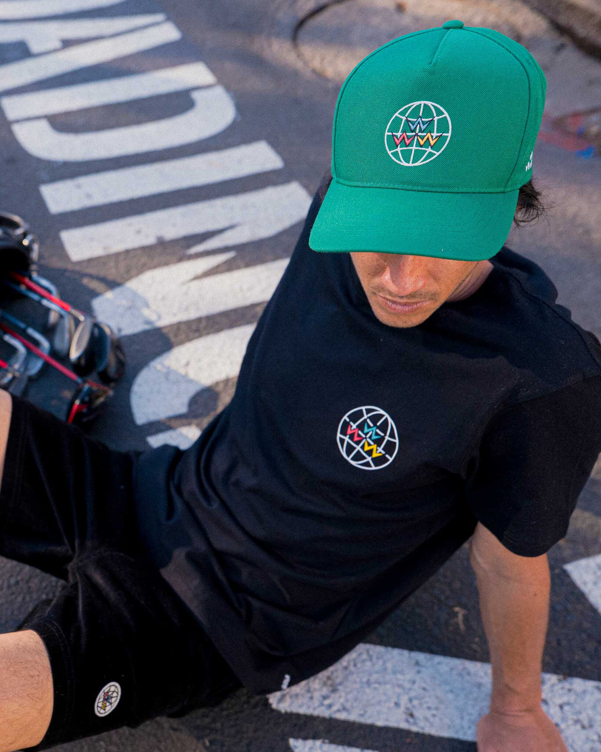 A man wearing a green snapback hat featuring a white globe graphic with multicolored V shapes.
