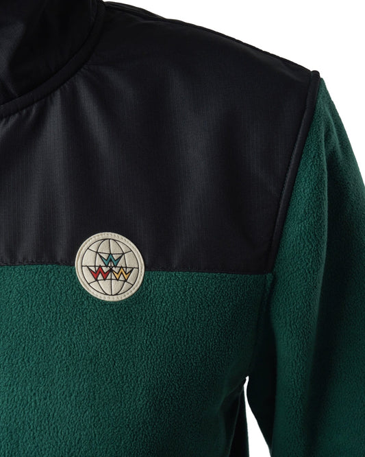Detail of an amazon green fleece sweater with a black shoulder panel and a round globe logo patch.