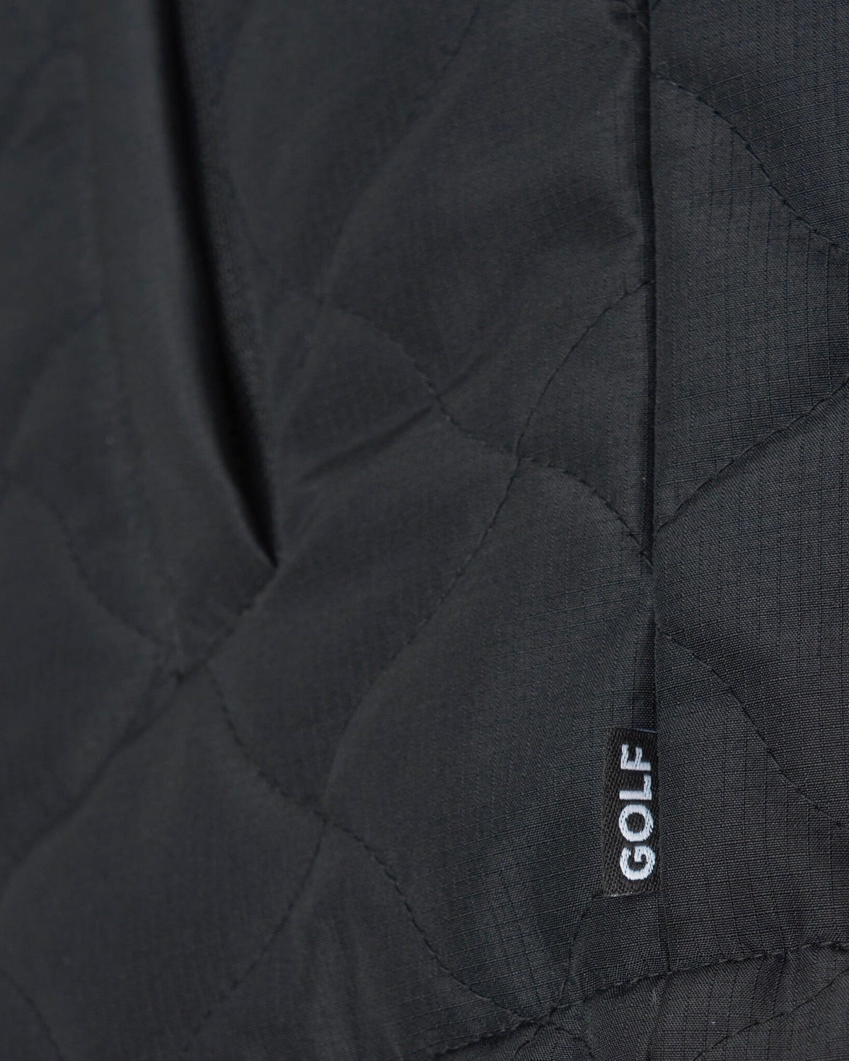 Detail of a black vest with warped argyle quilting, a side pocket, and a small tag reading GOLF.