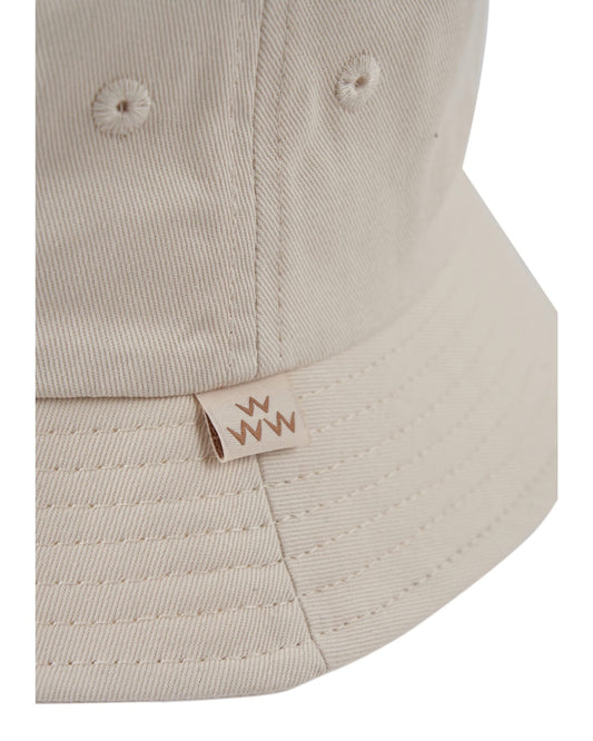 Detail of an off-white cotton bucket hat with topstitching and a small woven label featuring a crown logo.
