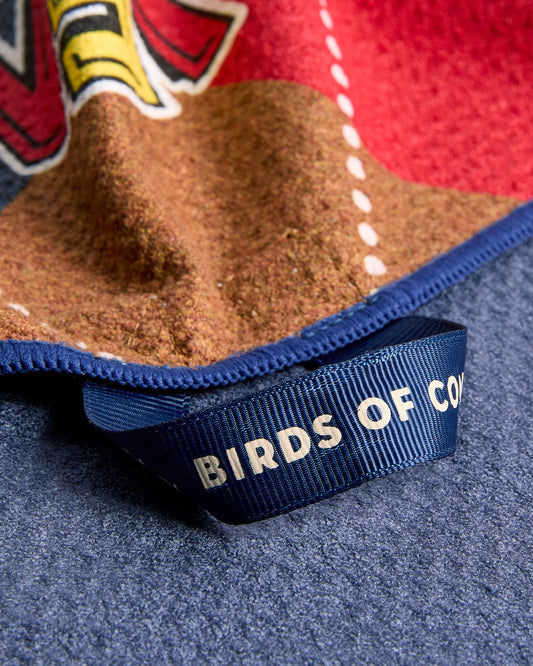 Detail of an argyle golf towel with red, brown, and blue panels, featuring a blue loop hanger with text.