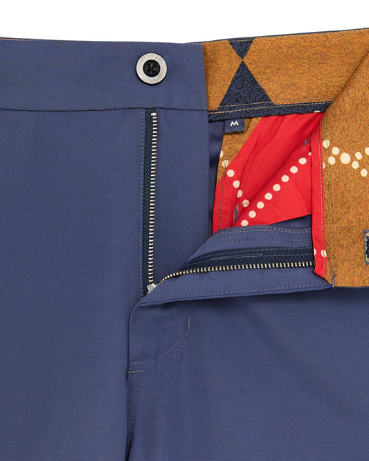 Detail of navy pants with a top button, belt loops, and an open fly revealing argyle print.
