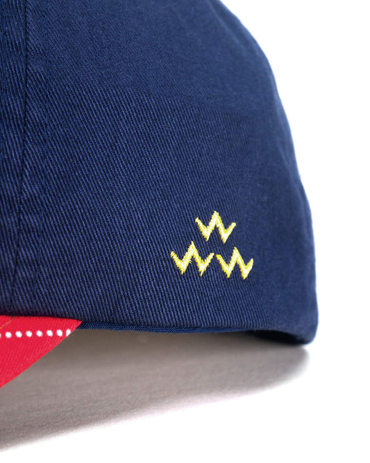 Detail of a navy cotton cap featuring a yellow embroidered logo and an argyle patterned brim edge.