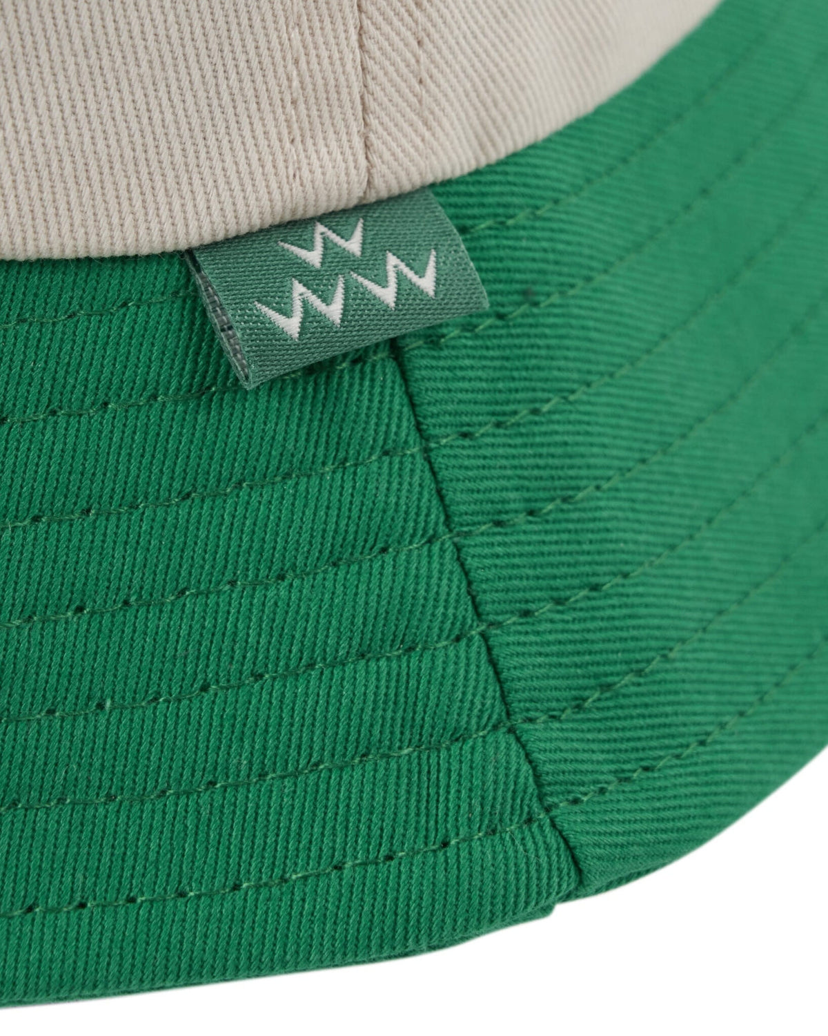 Detail of an off-white and green cotton bucket hat with a small green side tag featuring white teeth graphics.