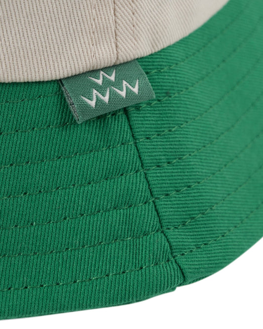 Detail of an off-white and green cotton bucket hat with a small green side tag featuring white teeth graphics.