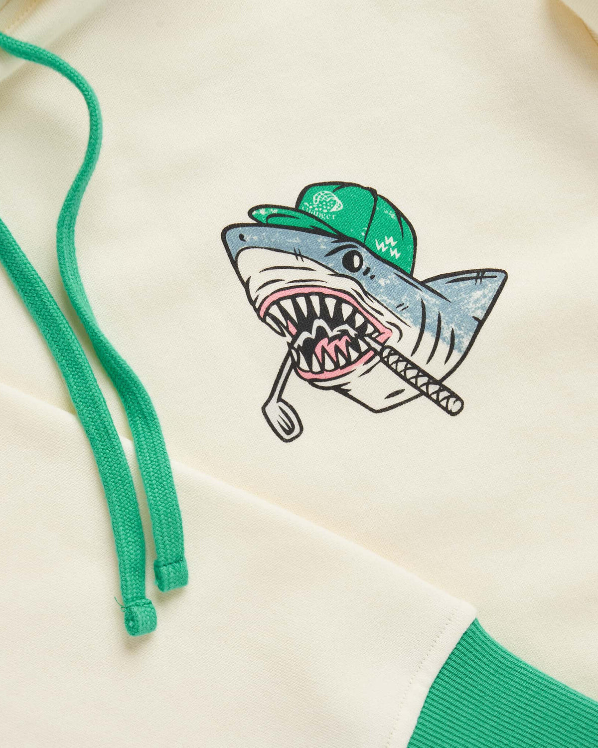 Detail of an antique white hoodie featuring a shark print graphic and green drawcords.