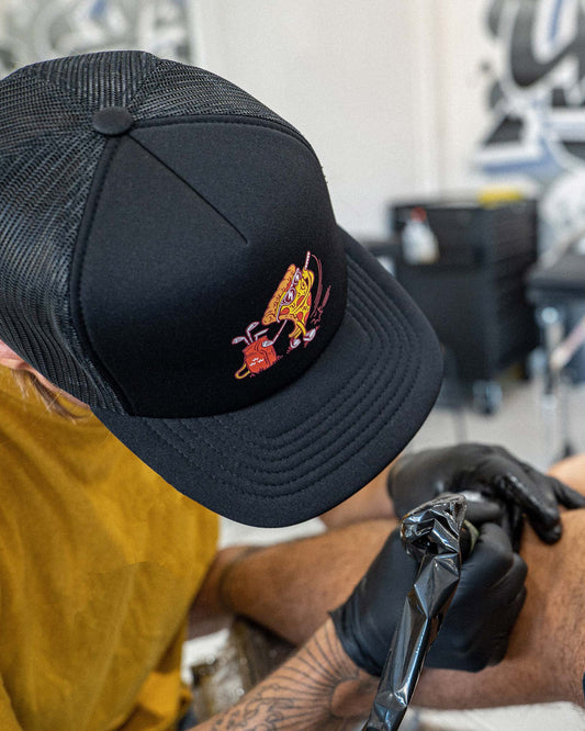 A person wearing a black trucker snapback with a curved brim and a pizza slice graphic on the front.