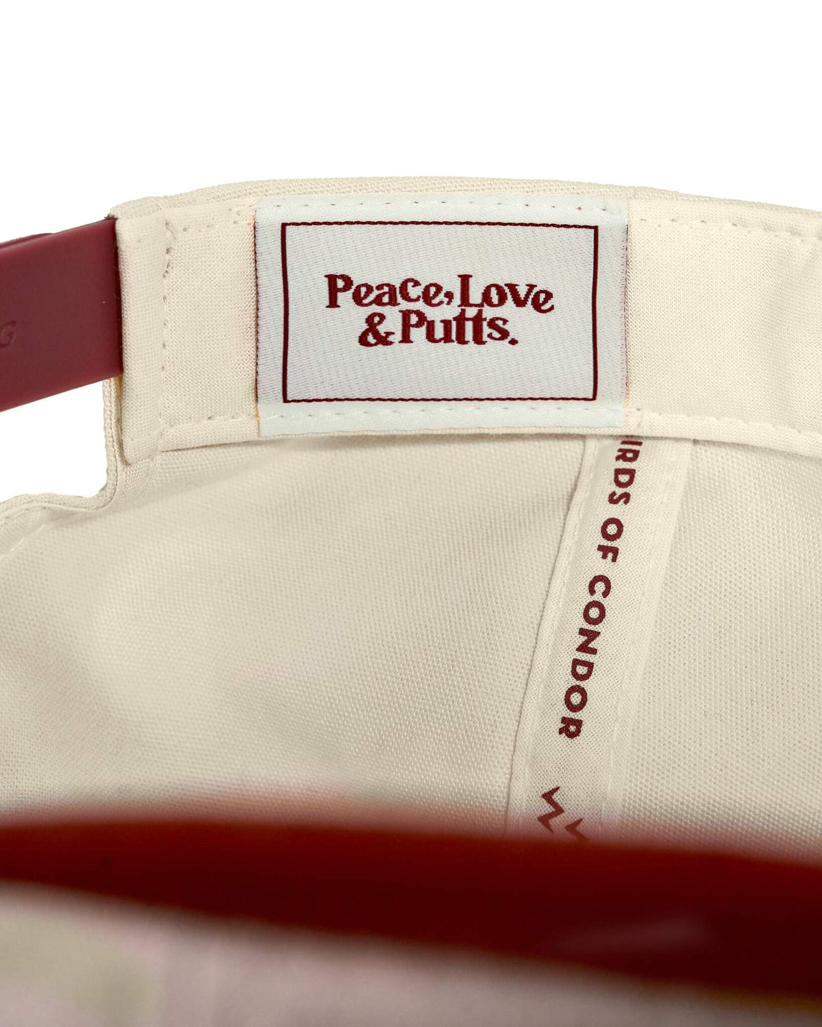 Detail of the interior label on a red wine and natural snapback featuring a Peace, Love & Putts. logo.