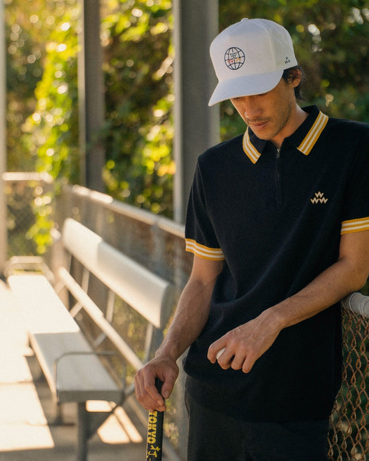 A man wearing a black polo shirt with yellow-striped collar and cuffs, and a triple eagle chest logo.
