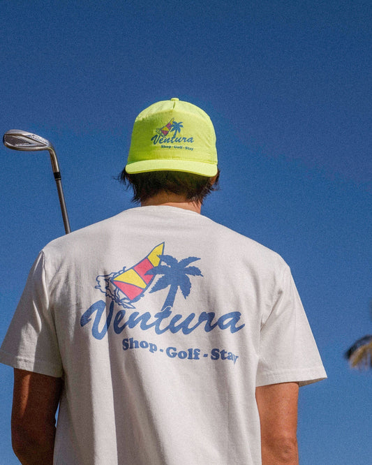 Back of a man wearing a white t-shirt and neon yellow cap, with a blue Ventura palm tree sail graphic.
