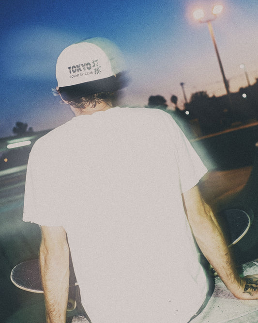 A person from behind wearing a white snapback with a black brim and a Tokyo Country Club front logo.