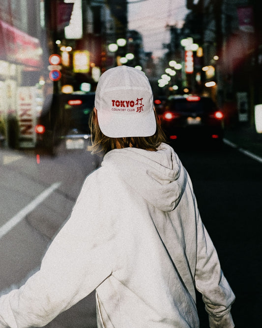 A person from behind wearing a white snapback with a red Tokyo Country Club logo print.