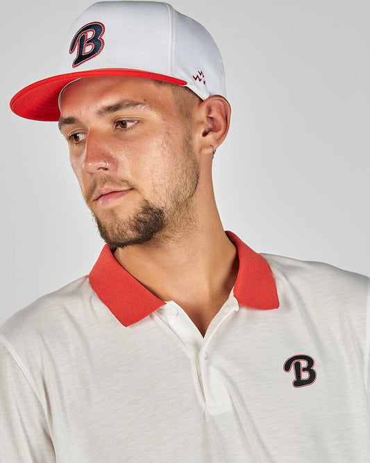 A man wearing a white cap with a red brim and a matching white polo shirt with a red collar.