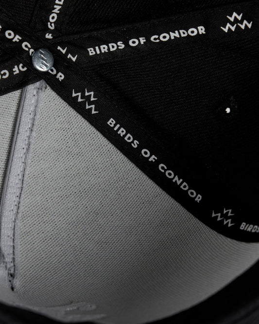 Detail of the inside of a black cap featuring branded internal taping and a metal button.