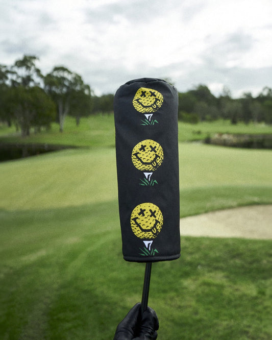 Black headcover featuring three stacked yellow smiley face golf ball graphics over green tees.