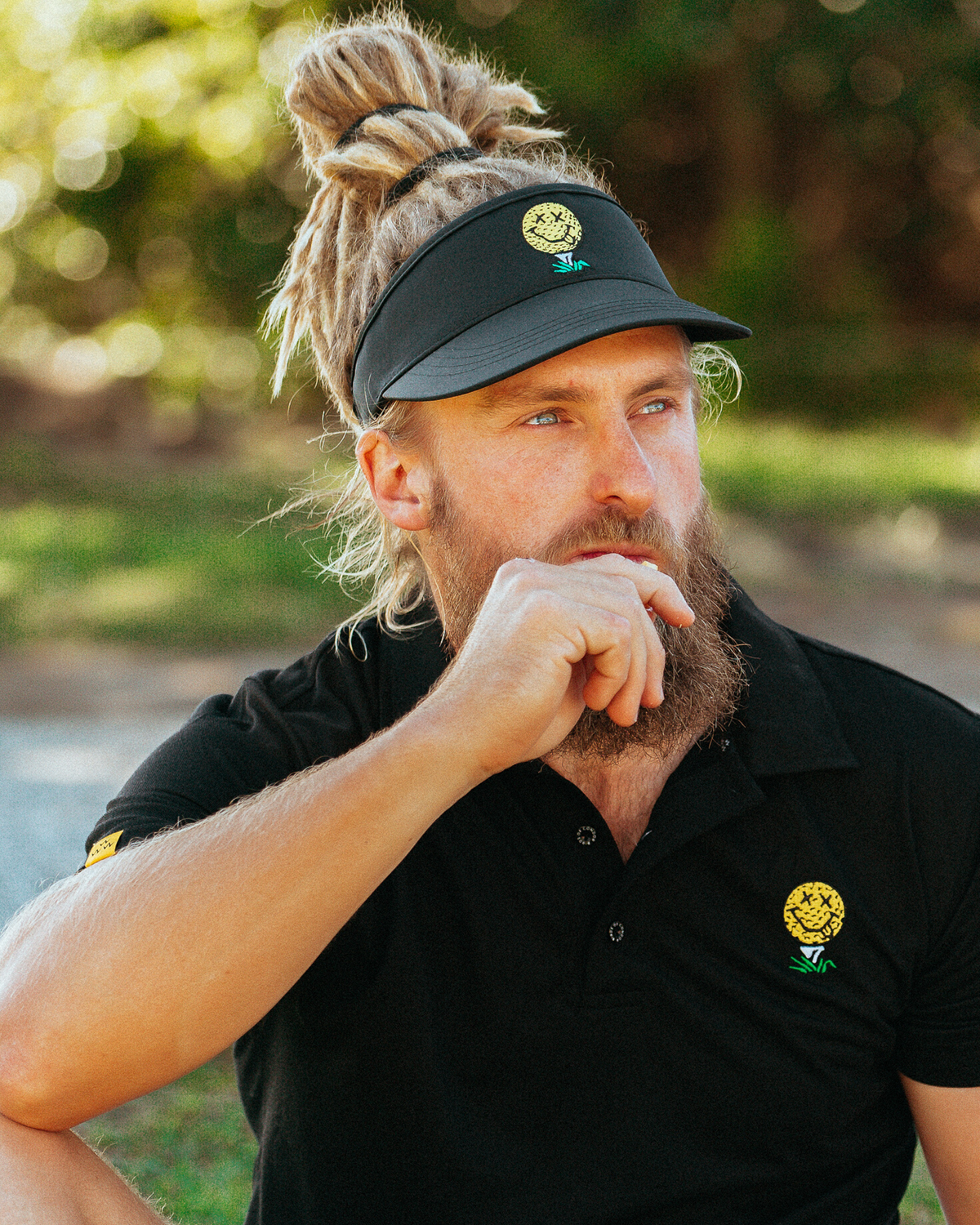 A man wearing a black visor featuring a yellow smiley face golf ball motif on the front crown.