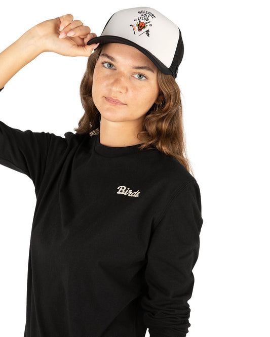 A person wearing a black and white trucker hat featuring a devil graphic and a black long-sleeve shirt.