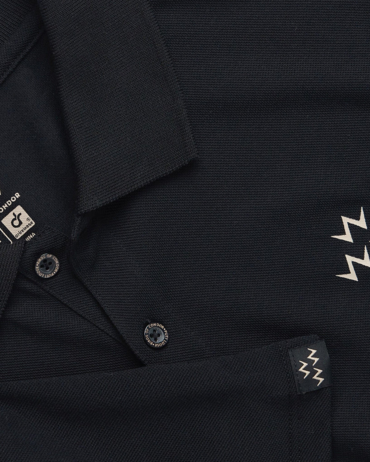 Detail of a black polo shirt featuring tan triple eagle print, collar, branded buttons, and sleeve logo.
