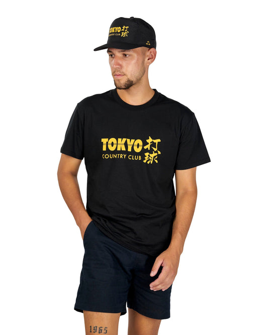 A man wearing a black t-shirt with a yellow Tokyo Country Club graphic, black shorts, and a matching cap.