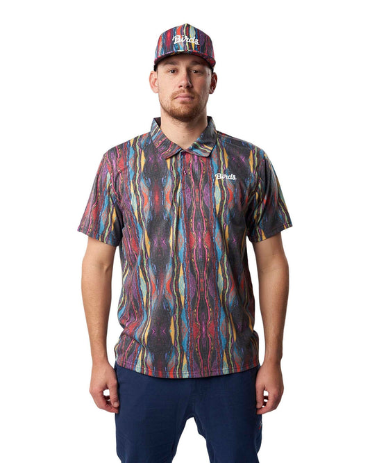 A man wearing a multi-coloured Coogi print polo shirt with a white script logo on the left chest and matching cap.