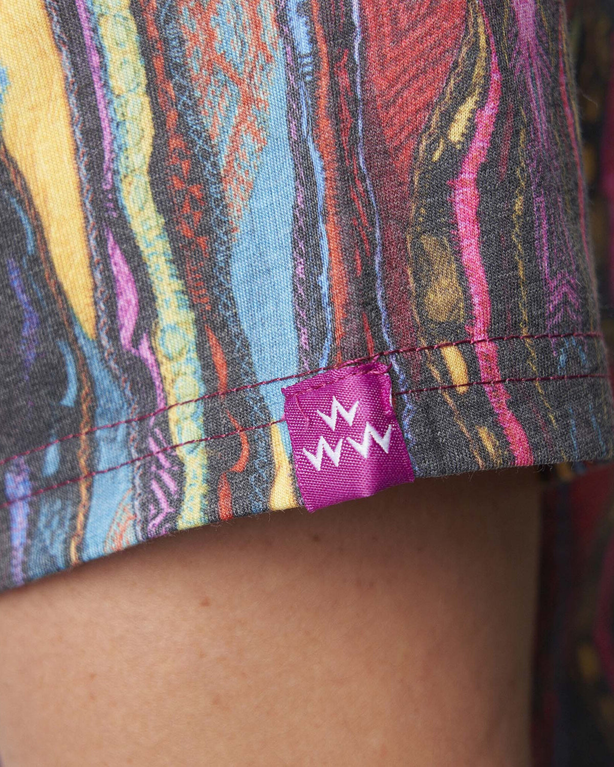 Detail of a Coogi print polo shirt showing a sleeve hem with a small purple branded tag.