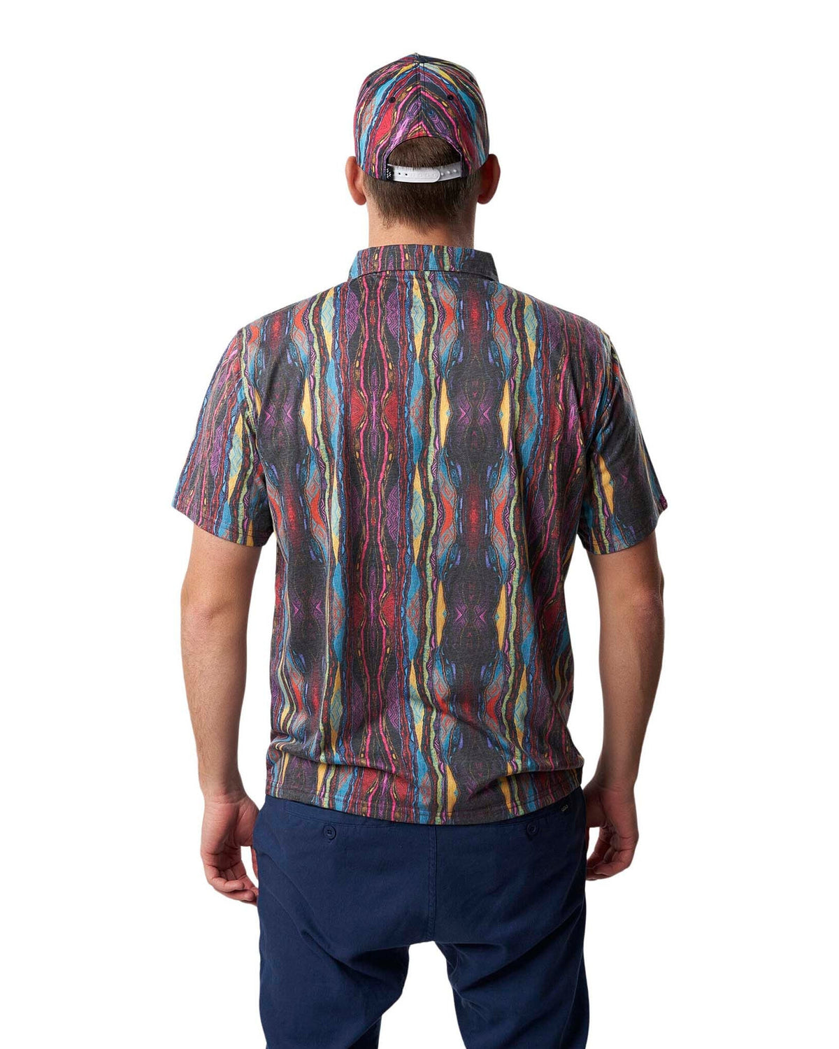 Back of a person wearing a multi-coloured print polo shirt, matching cap, and navy blue trousers.