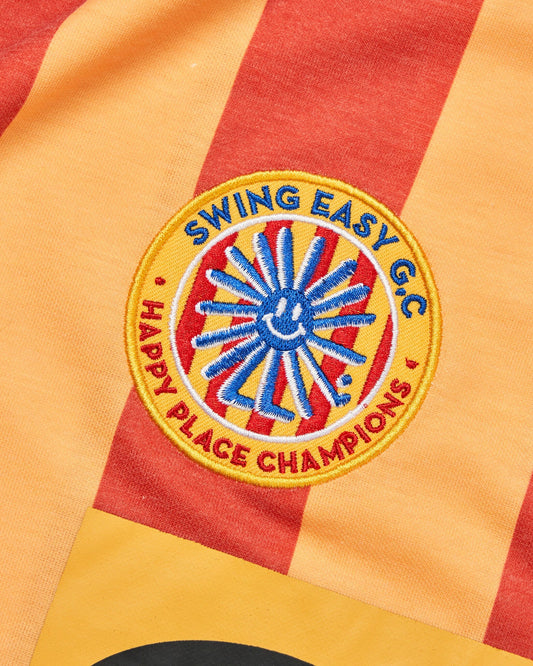 Detail of a red and yellow striped polo shirt with a round woven patch featuring a smiling sun motif.