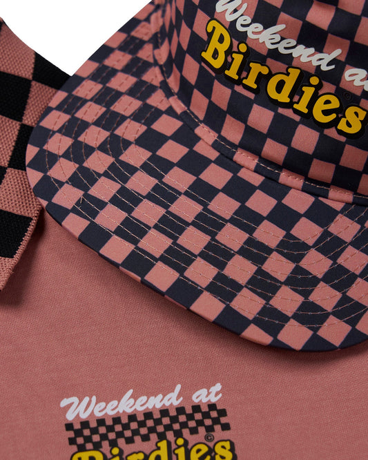 Detail of an old rose polo shirt and cap featuring a black checkered pattern and yellow Weekend at Birdies text.