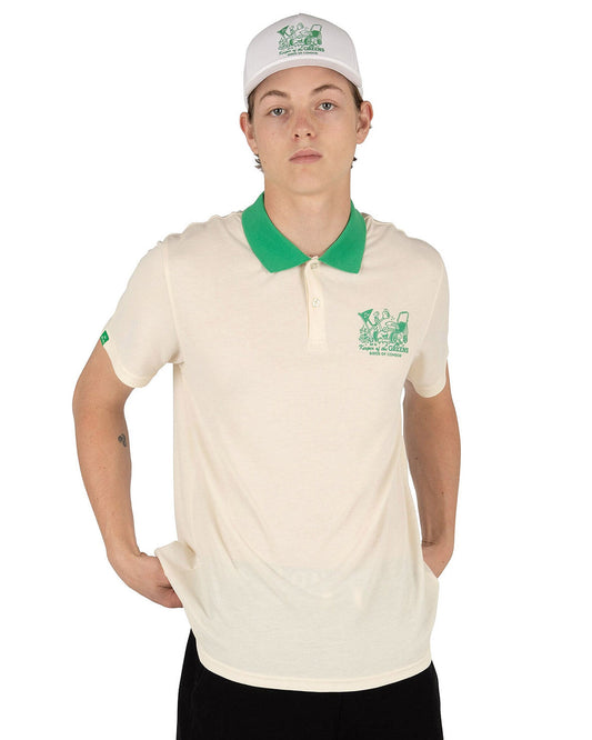 A man wearing a white snapback hat and a cream polo shirt with a green collar and chest graphic.