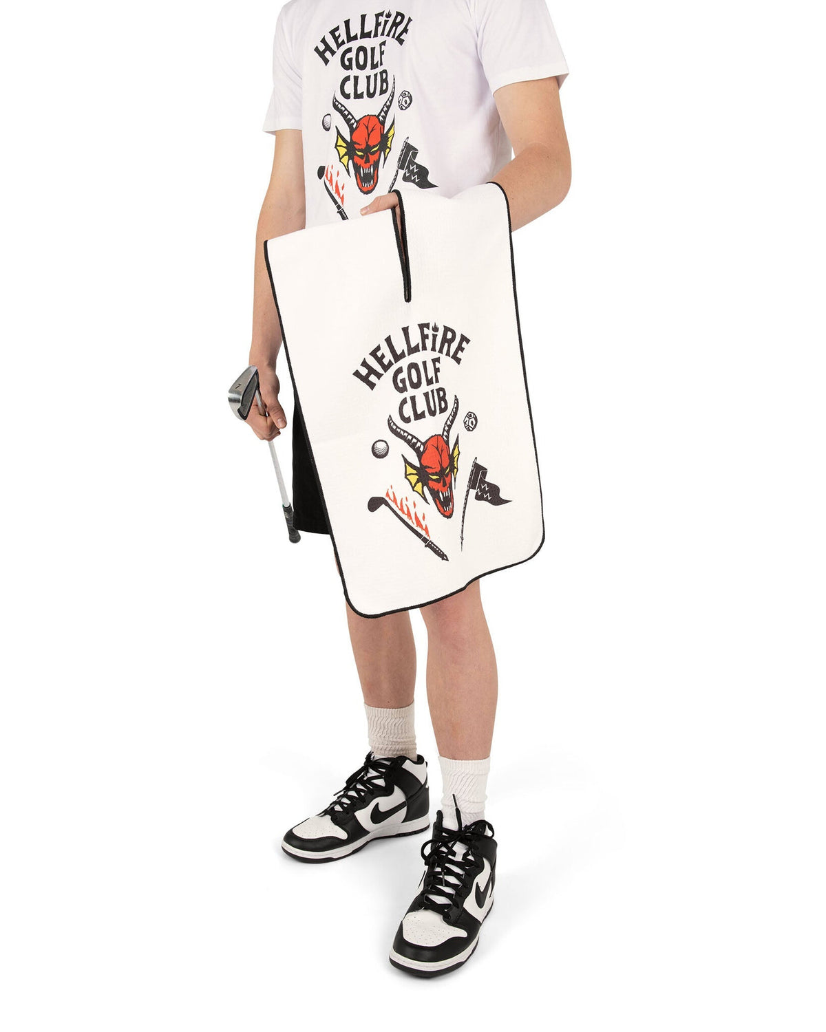 A person holding a white Hellfire Golf Club golf towel with a central hanging slit and a horned red demon graphic.