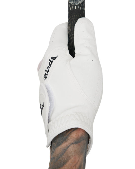 A hand wearing a white golf glove with black Birds script gripping a putter handle.