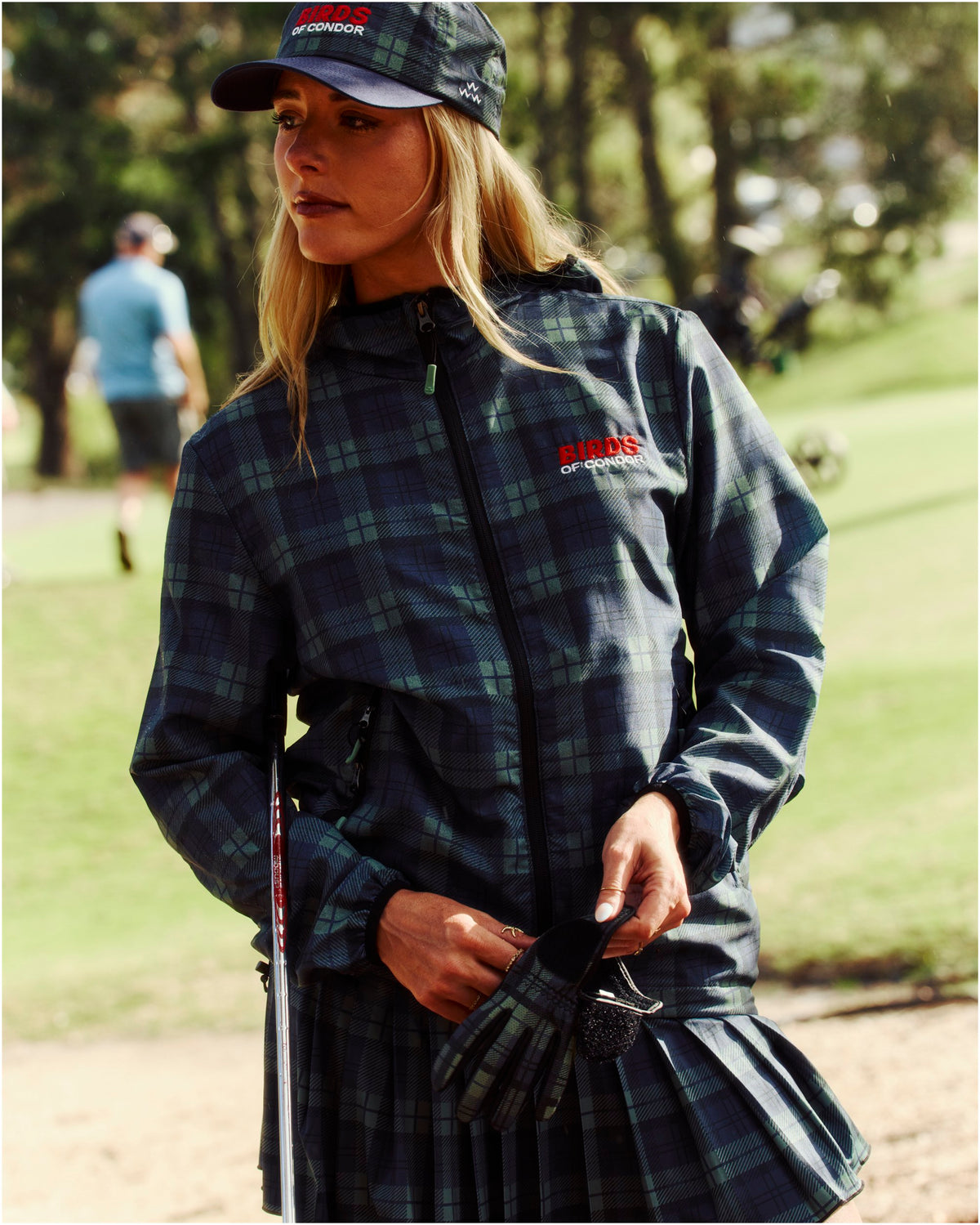 A woman wearing a blue and green plaid shell jacket with a zipped front and embroidered chest logo.
