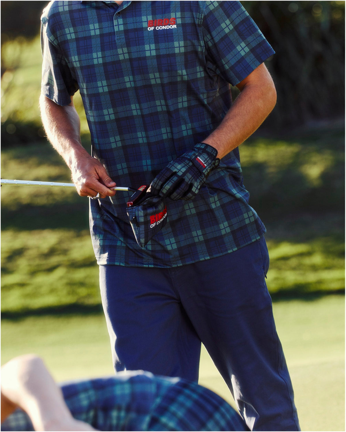 A man wearing a blue and green plaid polo shirt with a red logo on the chest.